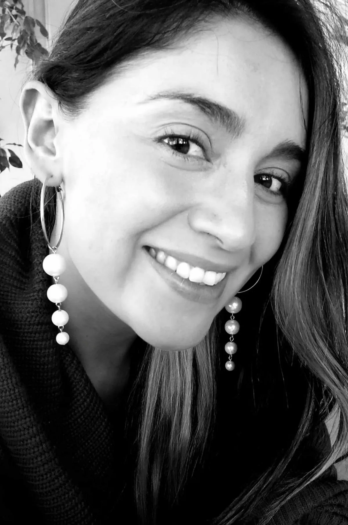 Black-and-white portrait of Daniela Jinés smiling, wearing pearl drop earrings