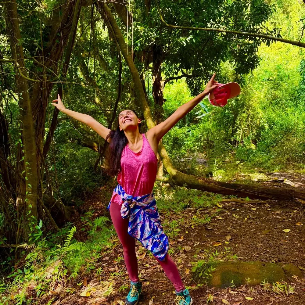 Daniela with arms stretched wide on a lush forest trail