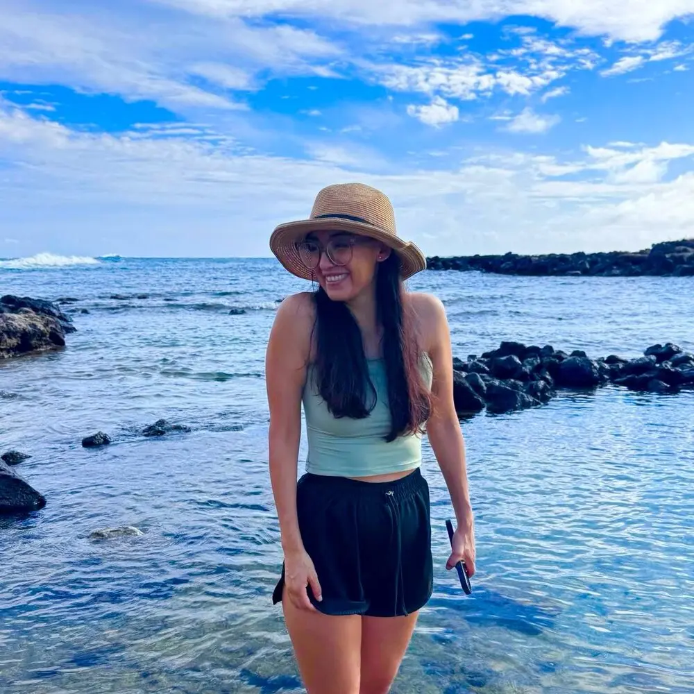 Daniela in a straw hat beside a rocky ocean shoreline