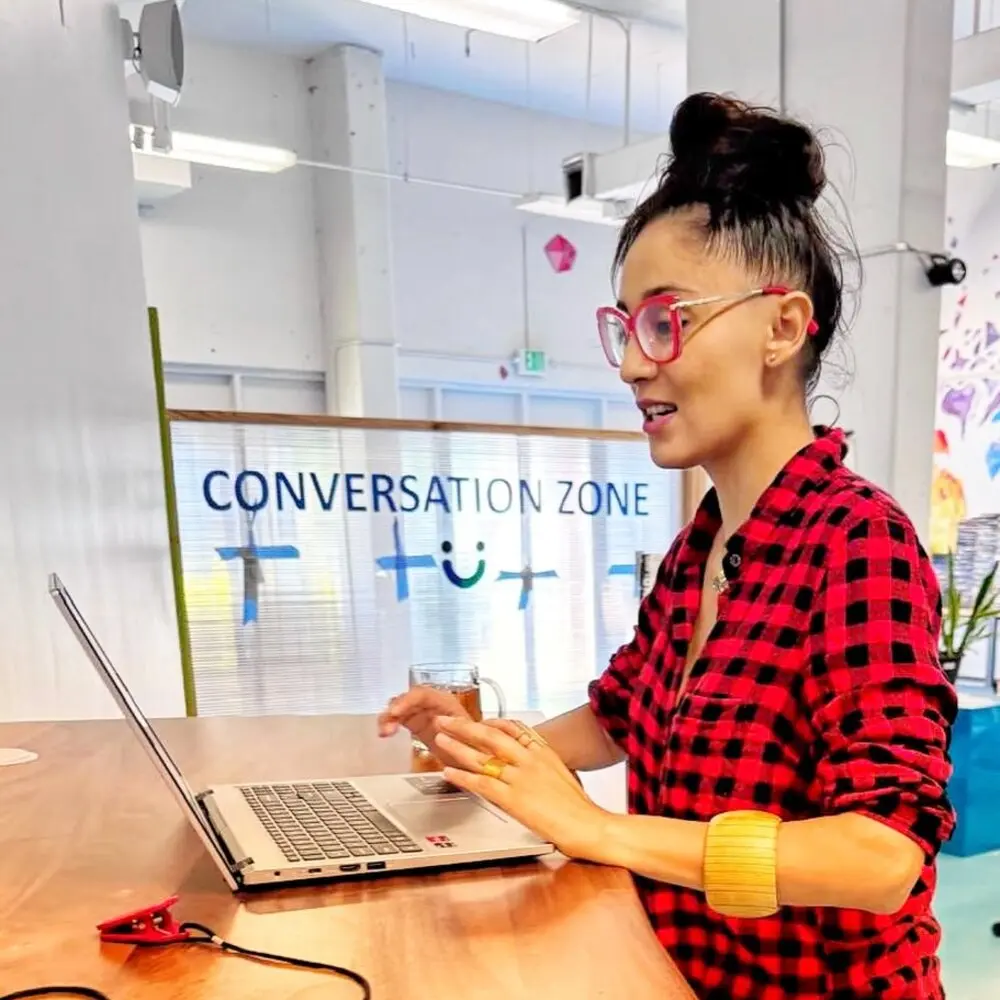 Daniela working on a laptop in a conversation zone, smiling mid-discussion
